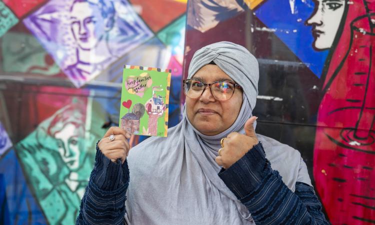 A woman holds a postcard with the slogan 'keep families together'