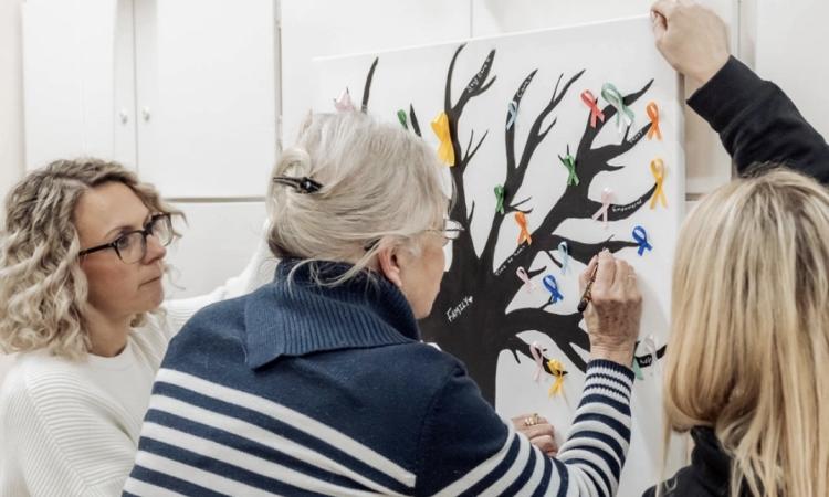 A women contributing to a tree artwork while two other women hold up the image