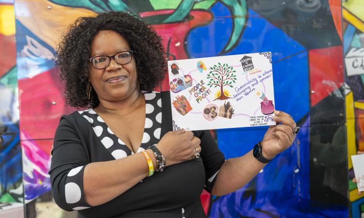 A woman hold a handmade peice of art depicting a tree and slogans
