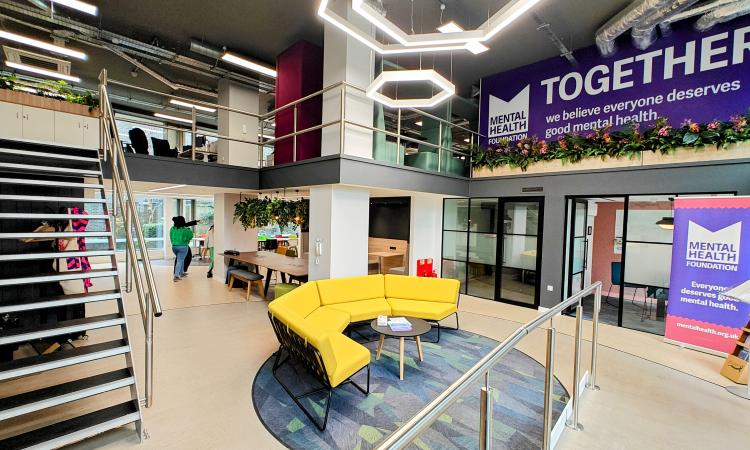 The inside of an office, on the left-hand side are stairs going up to a mezzanine, on the right is a large graphic with the Mental Health Foundation logo