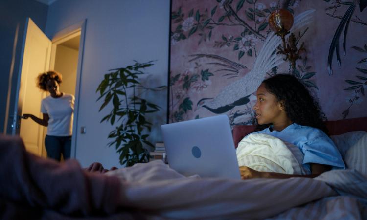 A mum stands in the doorway of her daughter's bedroom as she uses a laptop