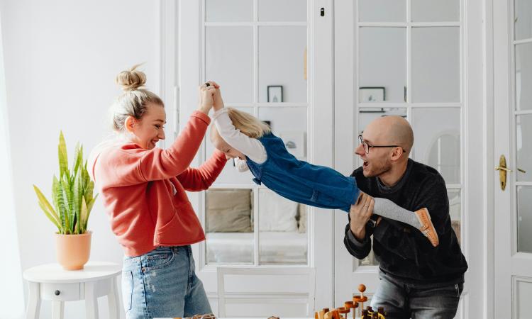 A man and woman playing with their daughter, carrying her as if she's flying through the air