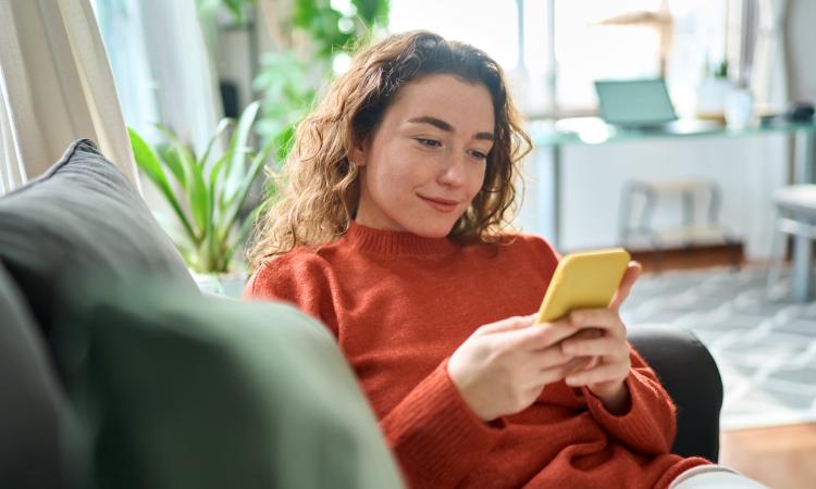 A woman sits on the sofa looking at her phone and smiling