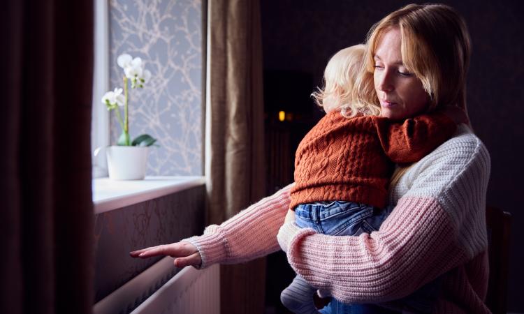 A woman holding a baby feels for heat from a radiator