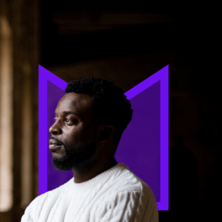 A Black man looking out of the window from a dark room.
