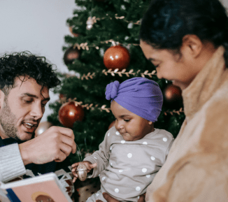 A family with a young child stood by a Christmas tree. 