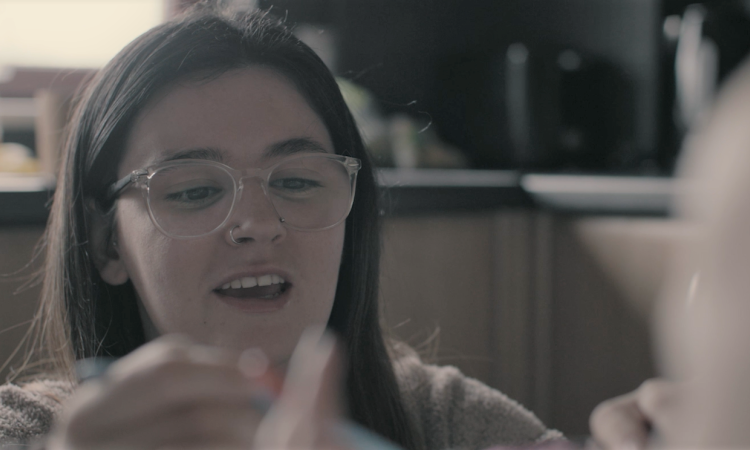 A woman wearing glasses, out of focus in the foreground is a baby